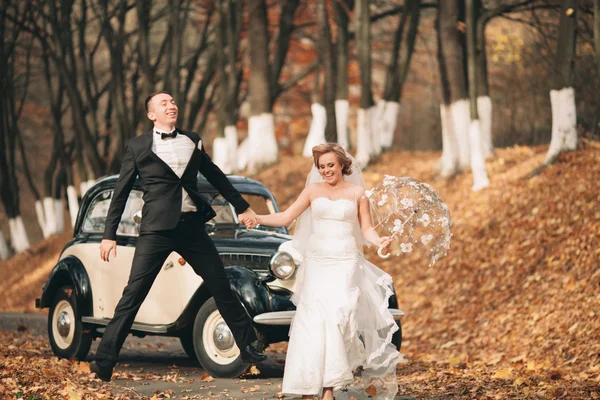 Pasangan pengantin, pengantin wanita, pria berciuman dan berpelukan di dekat mobil retro di musim gugur — Stok Foto