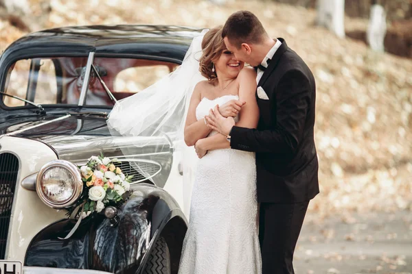 Stijlvolle bruidspaar, bruid, bruidegom zoenen en knuffelen in de buurt van retro auto in de herfst — Stockfoto