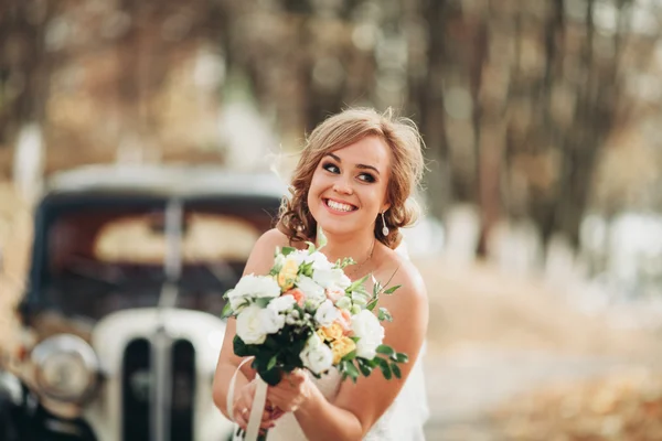 Belle mariée heureuse avec bouquet près de voiture rétro en automne — Photo