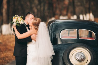 Şık düğün çift, Gelin, damat öpüşme ve retro arabanın yakınında sonbaharda sarılma