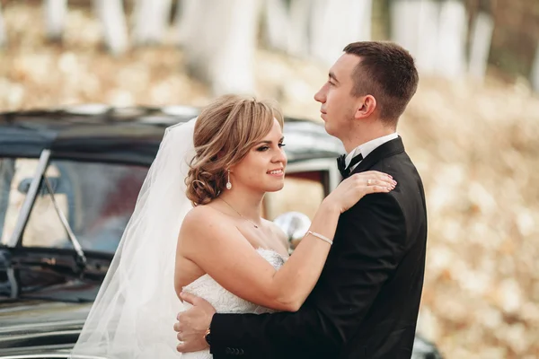 Stylish wedding couple, bride, groom kissing and hugging near retro car in autumn — Stock Photo, Image