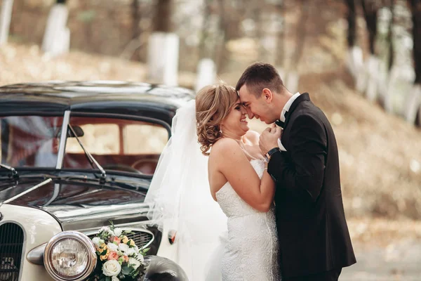 Stilvolles Hochzeitspaar, Braut, Bräutigam küssen und umarmen sich im Herbst in der Nähe von Retro-Autos — Stockfoto