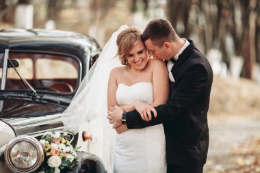 Şık düğün çift, Gelin, damat öpüşme ve retro arabanın yakınında sonbaharda sarılma