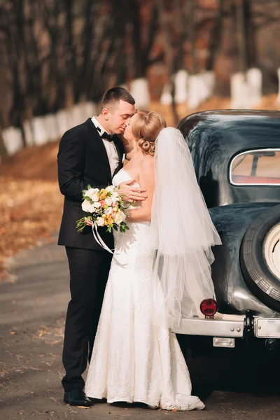 Elegante pareja de boda, novia, novio besándose y abrazándose cerca de coche retro en otoño — Foto de Stock