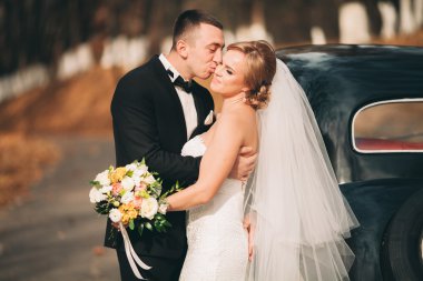 Şık düğün çift, Gelin, damat öpüşme ve retro arabanın yakınında sonbaharda sarılma