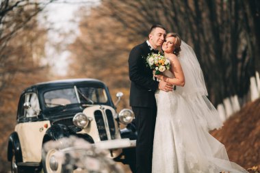 Şık düğün çift, Gelin, damat öpüşme ve retro arabanın yakınında sonbaharda sarılma
