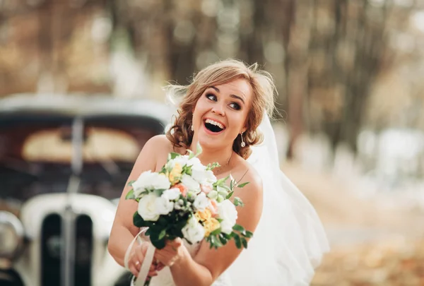 Bella sposa felice con bouquet vicino auto retrò in autunno — Foto Stock