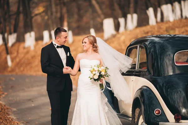 Elegante pareja de boda, novia, novio besándose y abrazándose cerca de coche retro en otoño — Foto de Stock