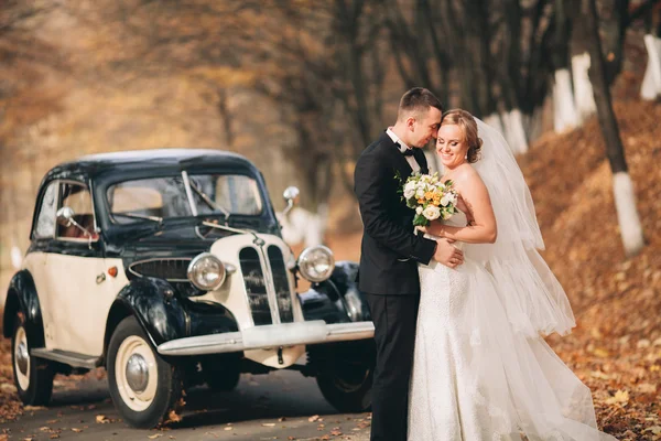 Casal de casamento elegante, noiva, noivo beijando e abraçando perto de carro retro no outono — Fotografia de Stock