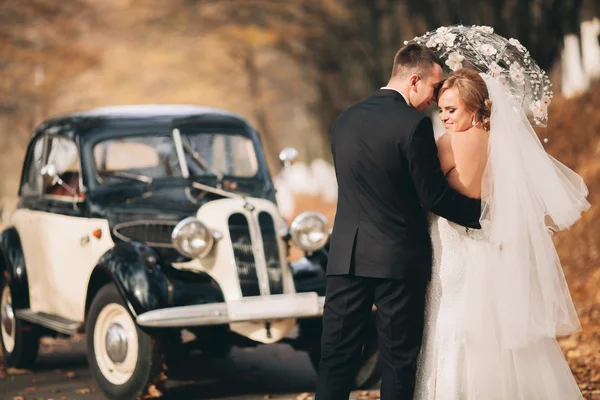 Stilvolles Hochzeitspaar, Braut, Bräutigam küssen und umarmen sich im Herbst in der Nähe von Retro-Autos — Stockfoto