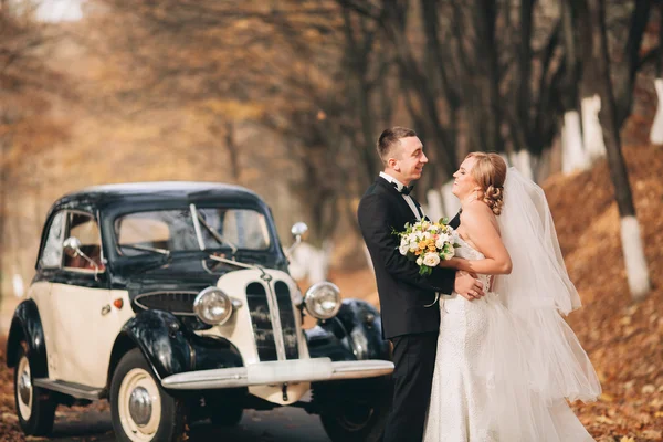 Elegante pareja de boda, novia, novio besándose y abrazándose cerca de coche retro en otoño — Foto de Stock