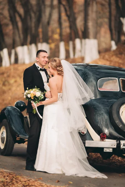 Elegante pareja de boda, novia, novio besándose y abrazándose cerca de coche retro en otoño — Foto de Stock