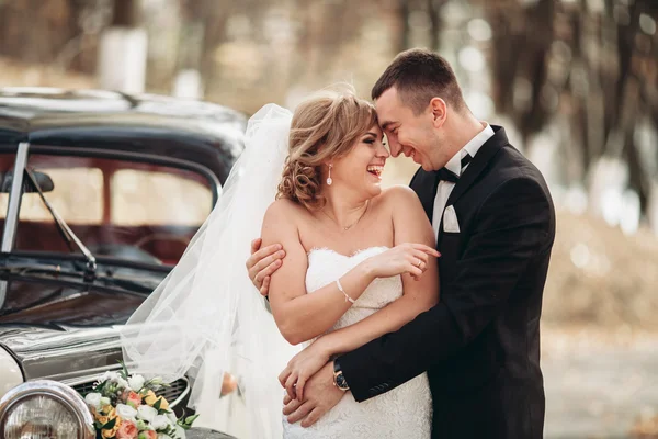 Stylowy ślub para, panny młodej, pana młodego, całowanie i przytulanie w pobliżu retro samochodów w jesieni — Zdjęcie stockowe