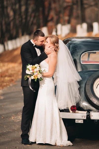 Stylish wedding couple, bride, groom kissing and hugging near retro car in autumn — Stock Photo, Image