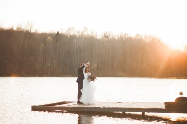 Zarif güzel düğün çifti bir göl kenarında günbatımında poz