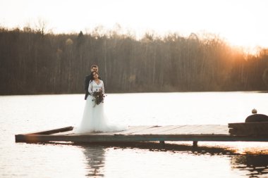 Zarif güzel düğün çifti bir göl kenarında günbatımında poz