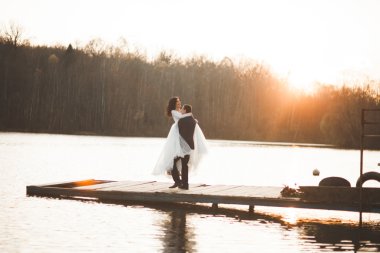 Zarif güzel düğün çifti bir göl kenarında günbatımında poz