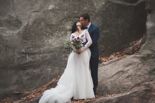 Прекрасная свадебная пара целуется и обнимается в лесу с большими камнями — стоковое фото