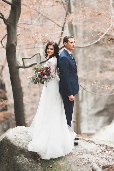 Hermosa pareja de boda besándose y abrazándose en el bosque con grandes rocas —  Fotos de Stock