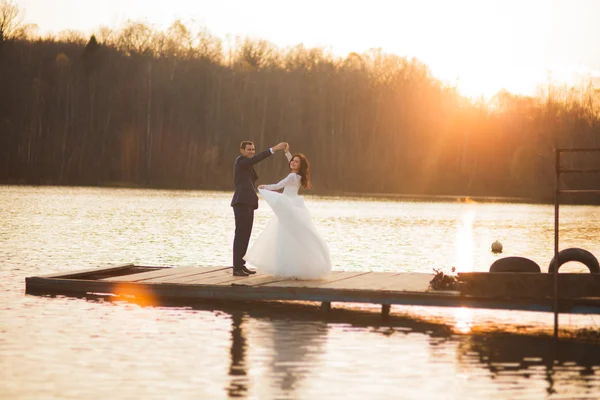 Zarif güzel düğün çifti bir göl kenarında günbatımında poz