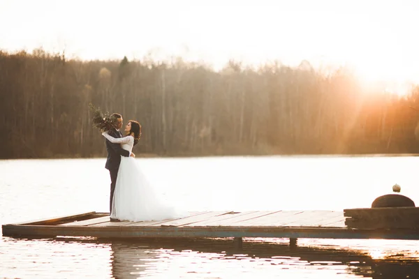 Elegante mooie bruidspaar poseren in de buurt van een meer bij zonsondergang — Stockfoto