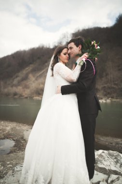 Öpüşme ve taşlarla Nehri yakınında kucaklayan güzel düğün çifti