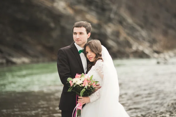 Verheugd huwelijksfeest paar, bruid en bruidegom poseren nette rivier tegen de achtergrond van de bergen — Stockfoto