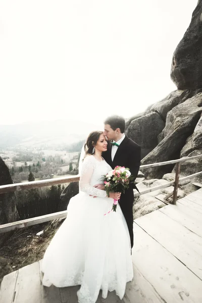 Verliebtes Hochzeitspaar küsst und umarmt sich in der Nähe von Felsen in schöner Landschaft — Stockfoto