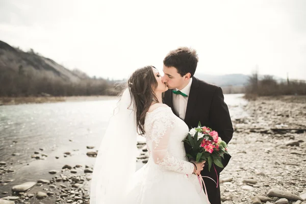 Όμορφο γαμήλιο ζεύγος φιλί και αγκαλιάζει κοντά στο ποτάμι με πέτρες — Φωτογραφία Αρχείου