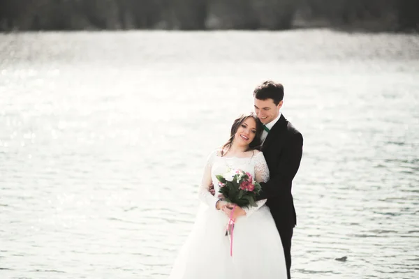 Gelukkig jonggehuwden, bruid en bruidegom poseren aan de rivier met mooi uitzicht — Stockfoto
