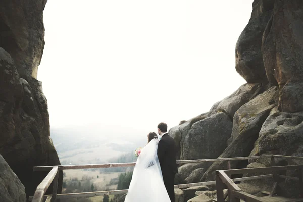 Bröllopspar i kärlek kysser och kramar nära stenar på vackert landskap — Stockfoto