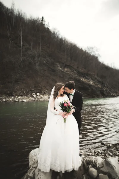 Öpüşme ve taşlarla Nehri yakınında kucaklayan güzel düğün çifti — Stok fotoğraf