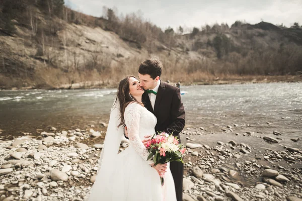 Glückliches Hochzeitspaar, Braut und Bräutigam posieren sauber Fluss vor der Kulisse der Berge — Stockfoto