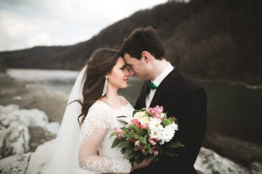 Öpüşme ve taşlarla Nehri yakınında kucaklayan güzel düğün çifti