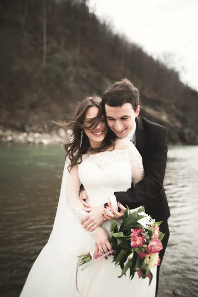 Casal de casamento feliz, noiva e noivo posando rio puro contra o pano de fundo das montanhas — Fotografia de Stock