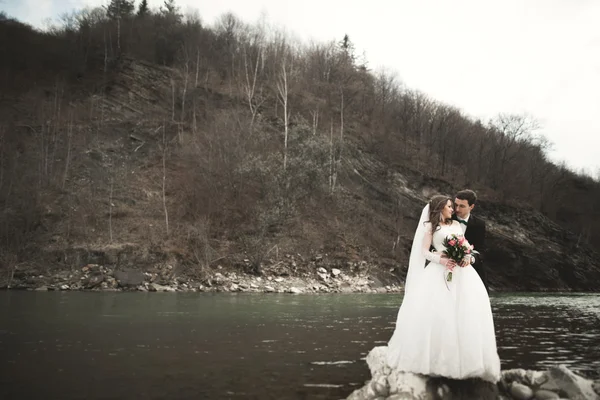 Glückliches Hochzeitspaar, Braut und Bräutigam posieren sauber Fluss vor der Kulisse der Berge — Stockfoto
