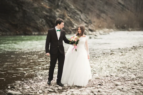 Hermosa pareja de boda besándose y abrazándose cerca del río con piedras —  Fotos de Stock