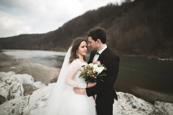 Happy wedding couple, bride and groom posing neat river against backdrop of the mountain — Stok Foto