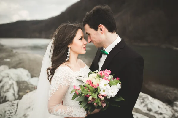 Hermosa pareja de boda besándose y abrazándose cerca del río con piedras —  Fotos de Stock