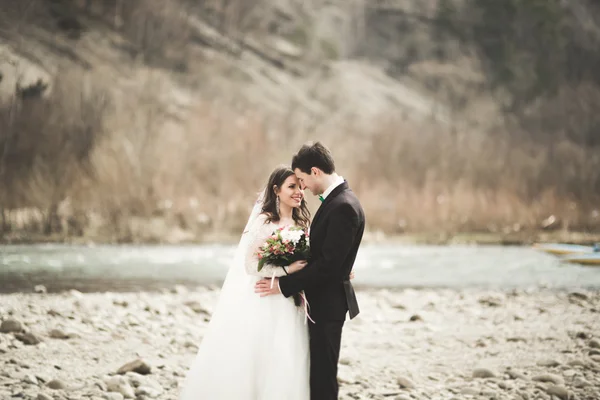 Casamento lindo casal beijando e abraçando perto do rio com pedras — Fotografia de Stock