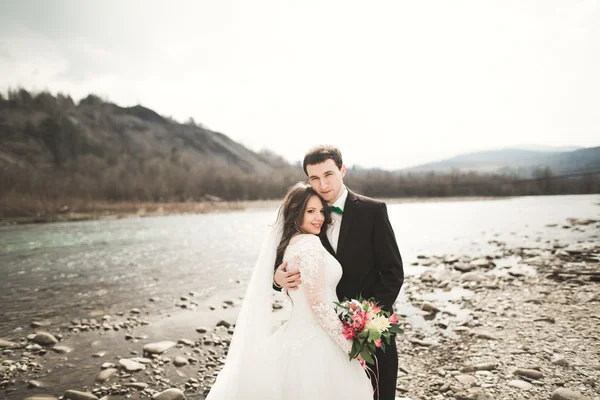 Szczęśliwy wesele para, Narzeczeni pozowanie czyste rzeki przeciw backdrop góry — Zdjęcie stockowe