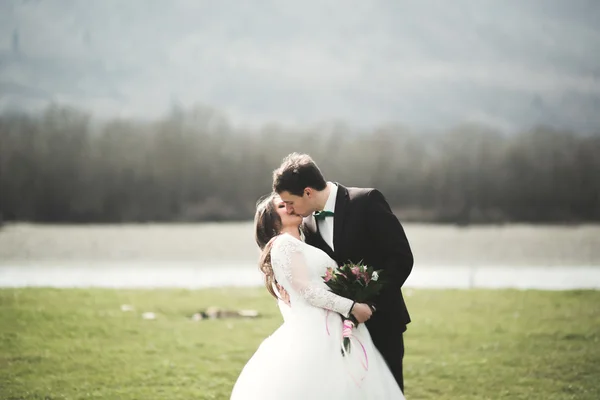 Beau couple de mariage, mariée, marié posant et marchant dans le champ sur le fond de hautes montagnes — Photo