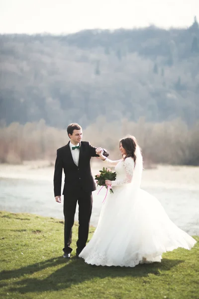 Pasangan pengantin yang cantik, pengantin wanita, berpose dan berjalan di lapangan dengan latar belakang pegunungan tinggi — Stok Foto