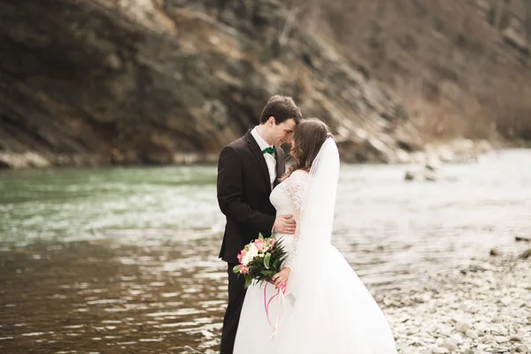Счастливая супружеская пара, невеста и жених позируют аккуратной рекой на фоне гор — стоковое фото