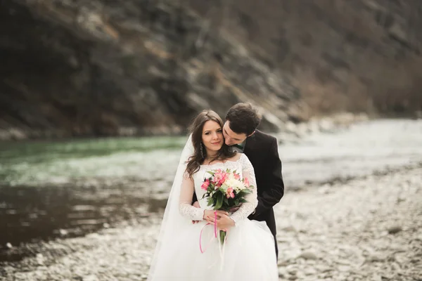 Casamento lindo casal beijando e abraçando perto do rio com pedras — Fotografia de Stock