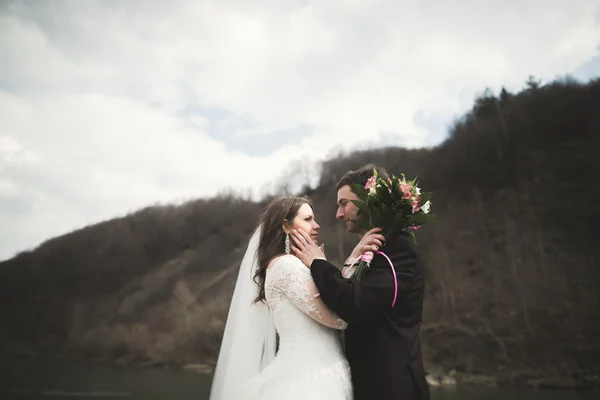 Beautifull wedding couple kissing and embracing near river with stones — Stock Photo, Image