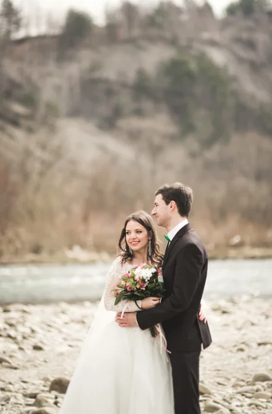 Hermosa pareja de boda besándose y abrazándose cerca del río con piedras —  Fotos de Stock