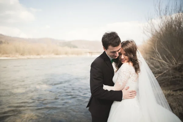 Boldog ifjú házasok, a menyasszony és a vőlegény pózol a folyó gyönyörű kilátással — Stock Fotó