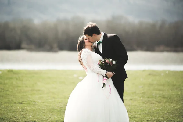 Casal de casamento bonito, noiva, noivo posando e andando em campo contra o fundo de altas montanhas — Fotografia de Stock