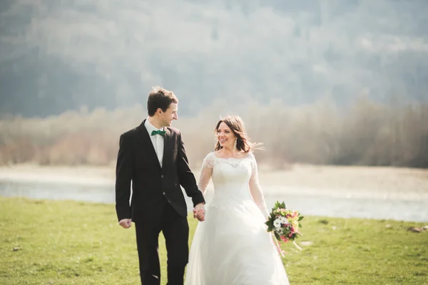 Hermosa pareja de boda, novia, novio posando y caminando en el campo sobre el fondo de las altas montañas — Foto de Stock